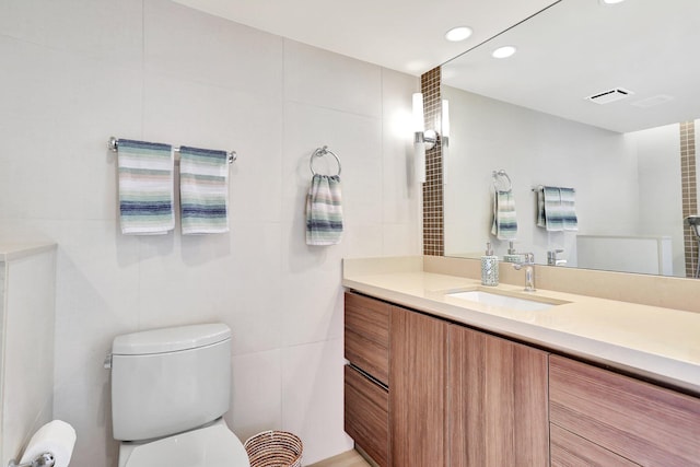 bathroom with vanity, toilet, and tile walls