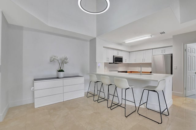 kitchen featuring a kitchen bar, kitchen peninsula, stainless steel appliances, sink, and white cabinets