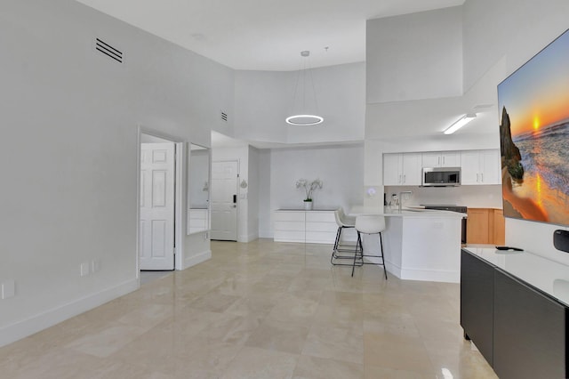 kitchen featuring a towering ceiling, a breakfast bar, stainless steel appliances, pendant lighting, and white cabinets