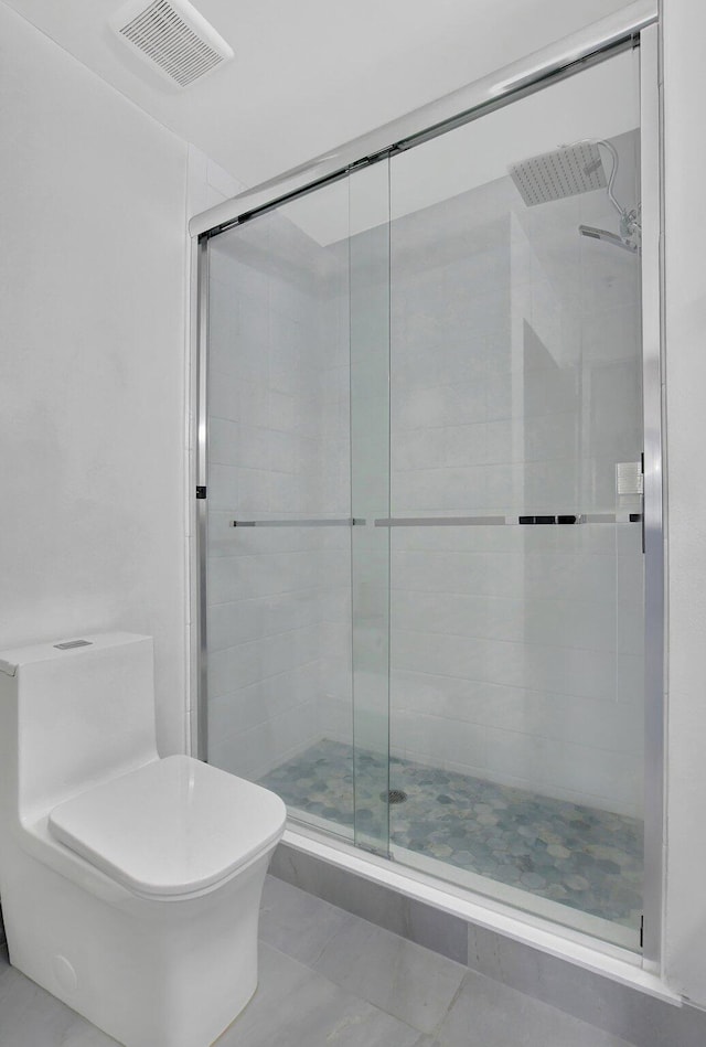 bathroom featuring tile patterned floors, a shower with shower door, and toilet