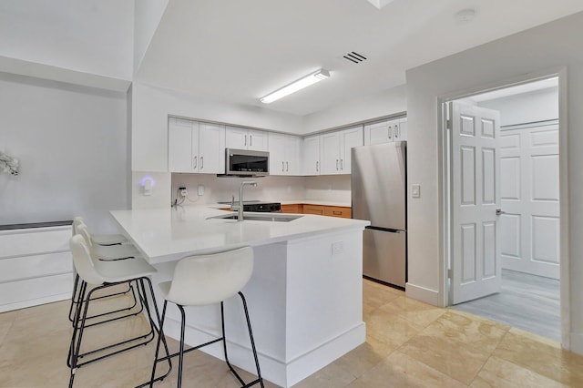 kitchen with a kitchen breakfast bar, sink, kitchen peninsula, white cabinetry, and stainless steel appliances