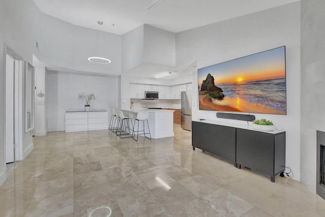 kitchen with pendant lighting, white cabinets, a towering ceiling, appliances with stainless steel finishes, and a kitchen bar