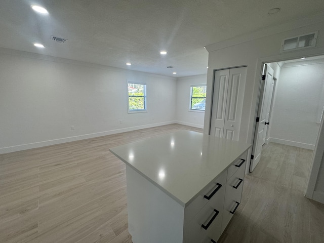 interior space with a kitchen island, light wood-type flooring, a textured ceiling, white cabinets, and ornamental molding