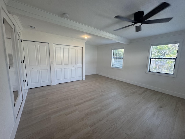 unfurnished bedroom with light hardwood / wood-style flooring, ceiling fan, a textured ceiling, beam ceiling, and multiple closets