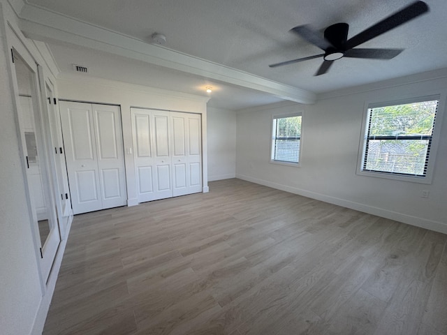 unfurnished bedroom with two closets, light hardwood / wood-style flooring, ceiling fan, a textured ceiling, and beam ceiling