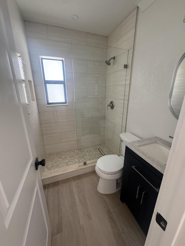 bathroom featuring vanity, toilet, wood-type flooring, and a tile shower