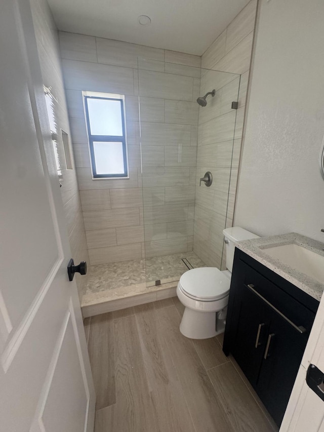 bathroom featuring hardwood / wood-style floors, vanity, toilet, and a tile shower