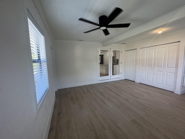 unfurnished bedroom featuring ceiling fan, wood-type flooring, ornamental molding, and multiple closets