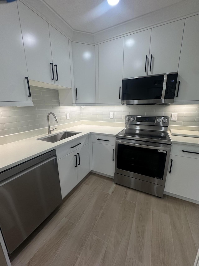 kitchen with appliances with stainless steel finishes, tasteful backsplash, sink, light hardwood / wood-style flooring, and white cabinetry