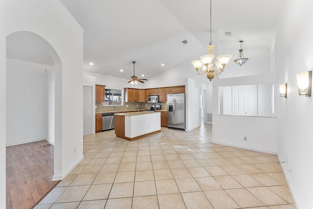 kitchen featuring a center island, backsplash, ceiling fan with notable chandelier, light tile patterned floors, and appliances with stainless steel finishes