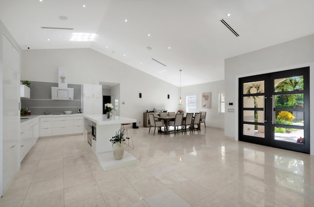 kitchen with french doors, high vaulted ceiling, a spacious island, decorative light fixtures, and white cabinets