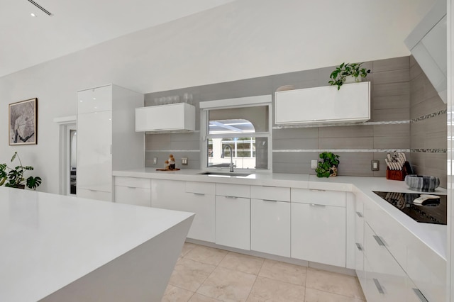 kitchen with white cabinets, sink, black electric cooktop, light tile patterned floors, and tasteful backsplash