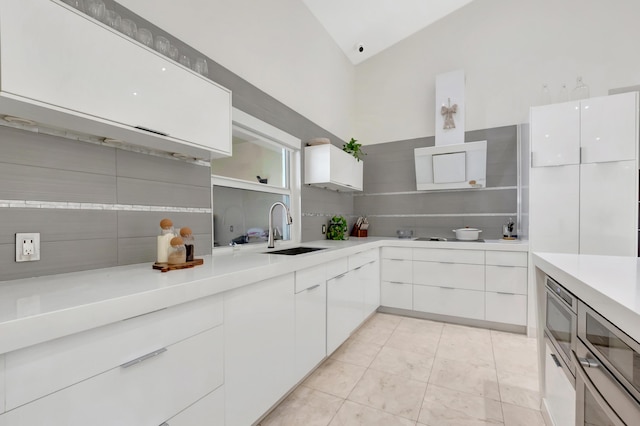 kitchen featuring vaulted ceiling, tasteful backsplash, white cabinetry, and sink