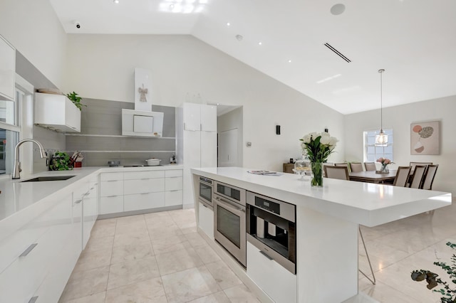 kitchen featuring white cabinetry, sink, hanging light fixtures, oven, and vaulted ceiling