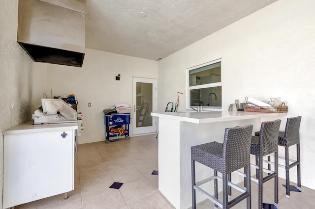 kitchen with kitchen peninsula, sink, white cabinetry, a breakfast bar area, and light tile patterned flooring