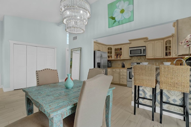 dining area with a high ceiling, light wood-type flooring, and an inviting chandelier