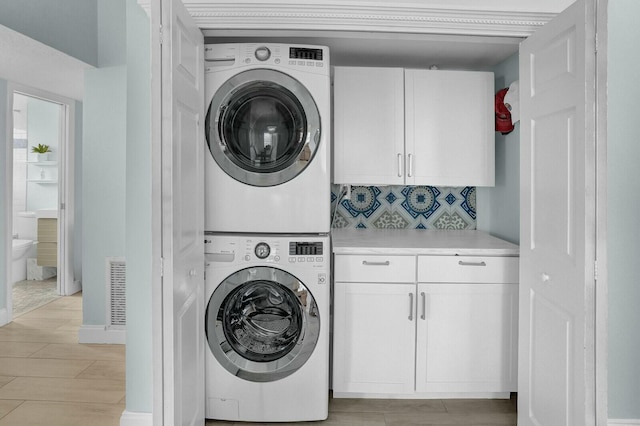 washroom featuring light hardwood / wood-style floors, cabinets, and stacked washing maching and dryer