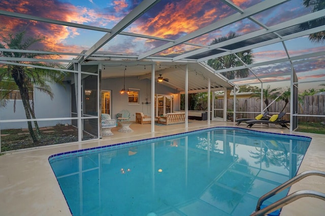 pool at dusk with outdoor lounge area, ceiling fan, a patio, and glass enclosure