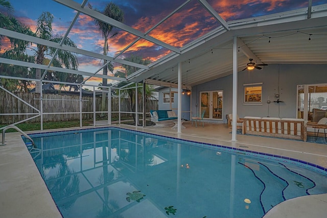 pool at dusk featuring glass enclosure, ceiling fan, outdoor lounge area, french doors, and a patio area