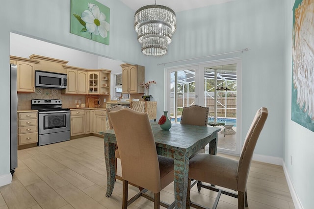 dining room with french doors, a towering ceiling, light hardwood / wood-style flooring, and a chandelier