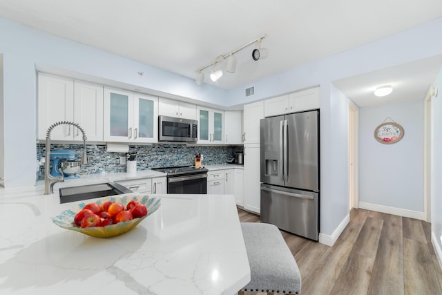 kitchen with appliances with stainless steel finishes, tasteful backsplash, sink, white cabinets, and light stone countertops