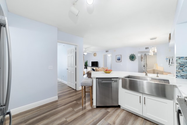 kitchen featuring pendant lighting, light hardwood / wood-style flooring, white cabinetry, stainless steel dishwasher, and kitchen peninsula