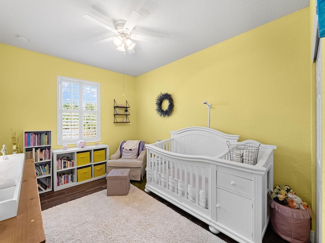 bedroom with hardwood / wood-style flooring, a crib, and ceiling fan