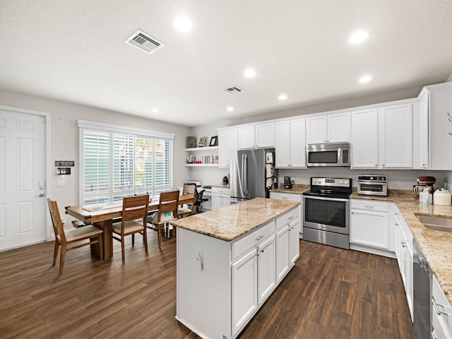 kitchen featuring white cabinetry, a center island, appliances with stainless steel finishes, dark hardwood / wood-style floors, and light stone countertops