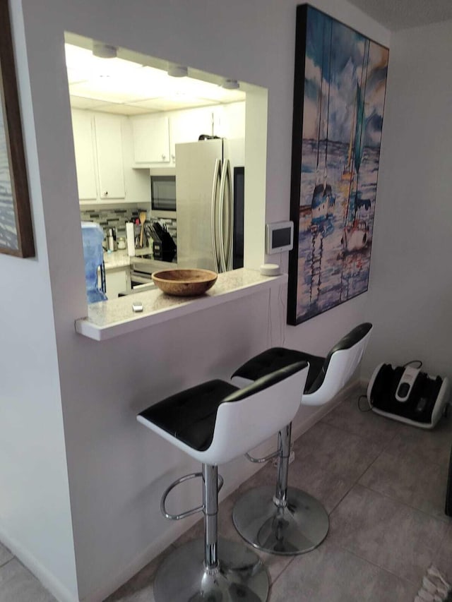 kitchen featuring white cabinetry, a kitchen breakfast bar, kitchen peninsula, stainless steel fridge, and white range with gas cooktop