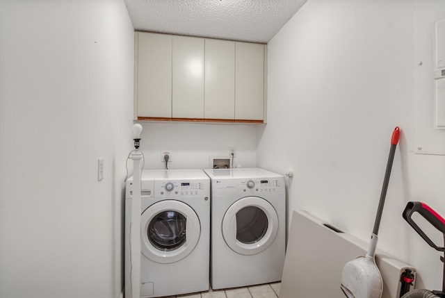 laundry room with cabinets, a textured ceiling, washer and clothes dryer, and light tile patterned flooring