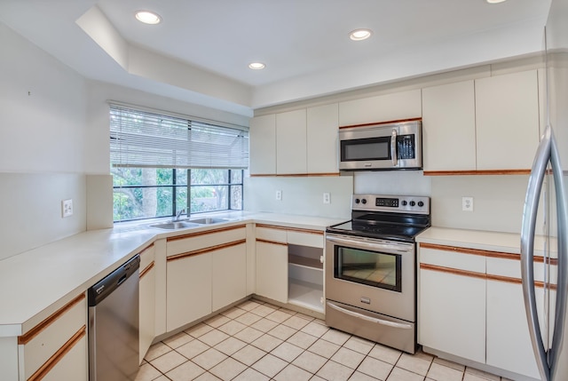 kitchen featuring white cabinets, sink, light tile patterned floors, a tray ceiling, and stainless steel appliances