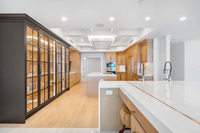 kitchen with stainless steel oven, a center island, sink, coffered ceiling, and light hardwood / wood-style floors