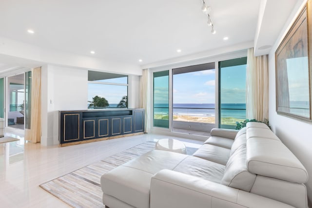 living room with a wealth of natural light, rail lighting, a water view, and expansive windows