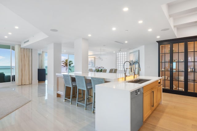 kitchen with ceiling fan, dishwasher, sink, a kitchen bar, and a center island with sink