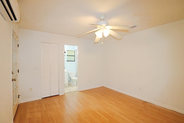 unfurnished bedroom featuring ensuite bathroom, an AC wall unit, light hardwood / wood-style flooring, ceiling fan, and a closet