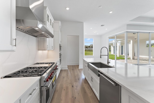 kitchen featuring white cabinets, wall chimney exhaust hood, sink, and appliances with stainless steel finishes