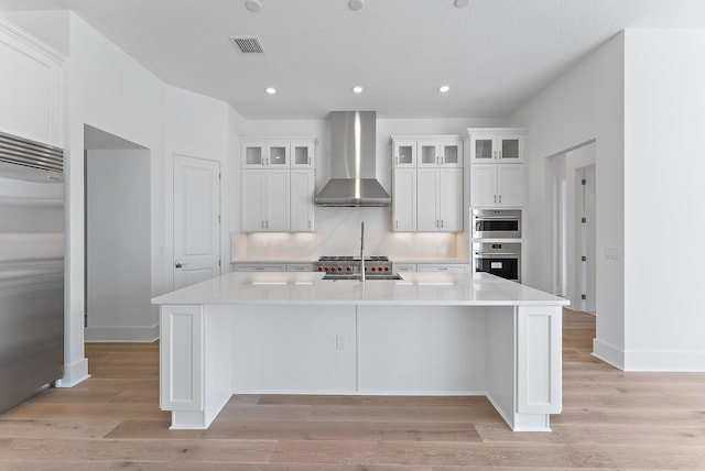 kitchen with white cabinets, appliances with stainless steel finishes, a spacious island, and wall chimney range hood