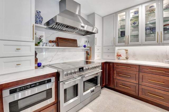 kitchen featuring white cabinetry, double oven range, wall chimney range hood, and backsplash