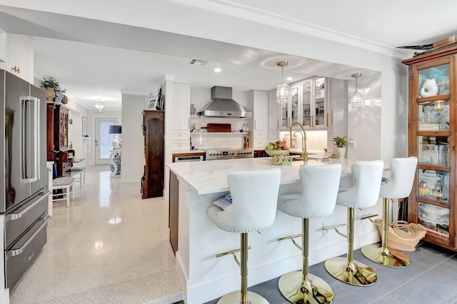 kitchen with white cabinetry, wall chimney exhaust hood, pendant lighting, a breakfast bar area, and appliances with stainless steel finishes