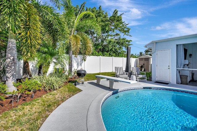 view of pool featuring a diving board, a grill, a patio area, and a shed