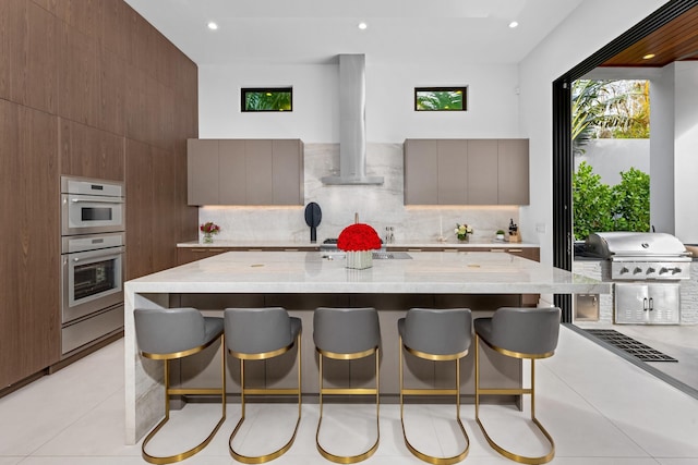 kitchen featuring range hood, light tile patterned floors, tasteful backsplash, and a breakfast bar area