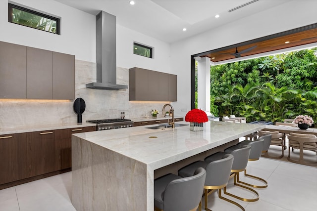 kitchen featuring sink, a kitchen island with sink, range hood, and light stone countertops