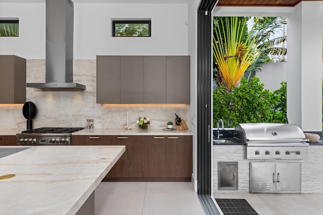 kitchen with stainless steel gas stovetop, wall chimney exhaust hood, dark brown cabinetry, sink, and tasteful backsplash