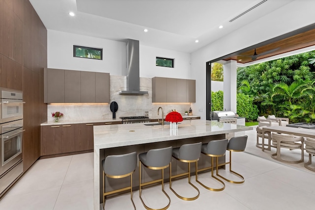 kitchen featuring sink, a kitchen breakfast bar, island exhaust hood, light stone countertops, and a center island with sink