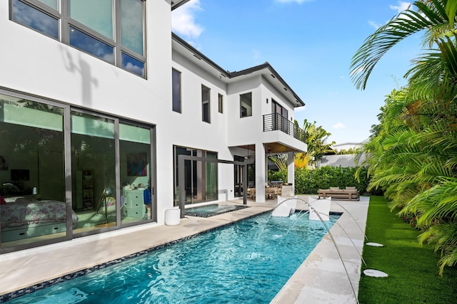 rear view of house with a balcony, a swimming pool with hot tub, an outdoor living space, and a patio