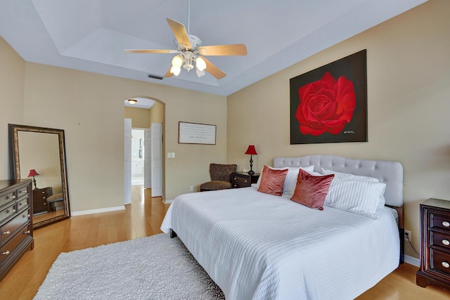 bedroom featuring a raised ceiling, ceiling fan, and light wood-type flooring