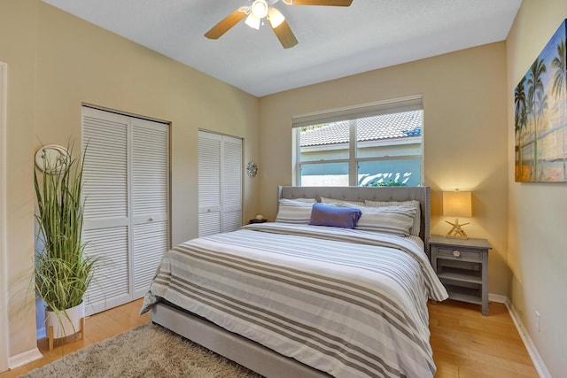 bedroom with light wood-type flooring, ceiling fan, and multiple closets