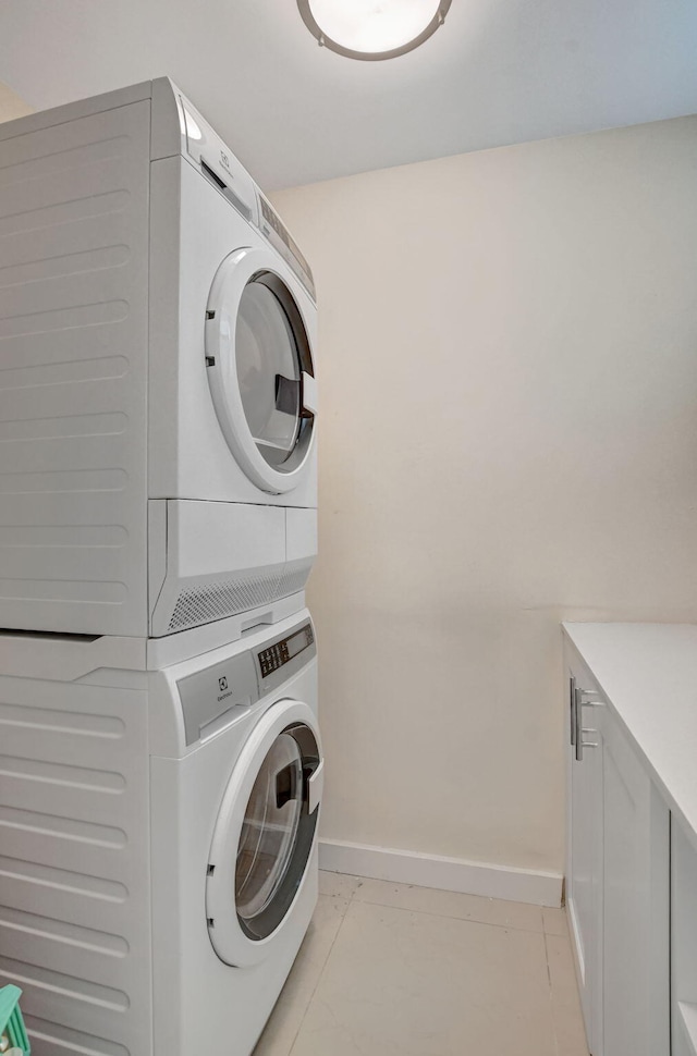 washroom with light tile patterned floors, cabinets, and stacked washer / drying machine