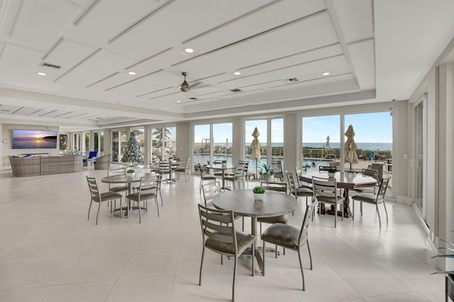 tiled dining area with ceiling fan, a water view, and a tray ceiling