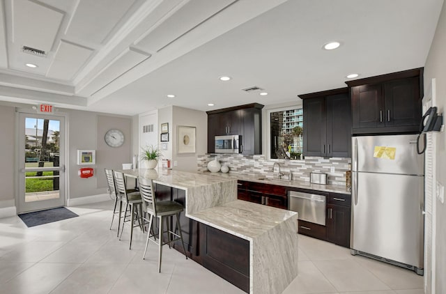 kitchen with a center island, sink, light stone countertops, a kitchen bar, and stainless steel appliances